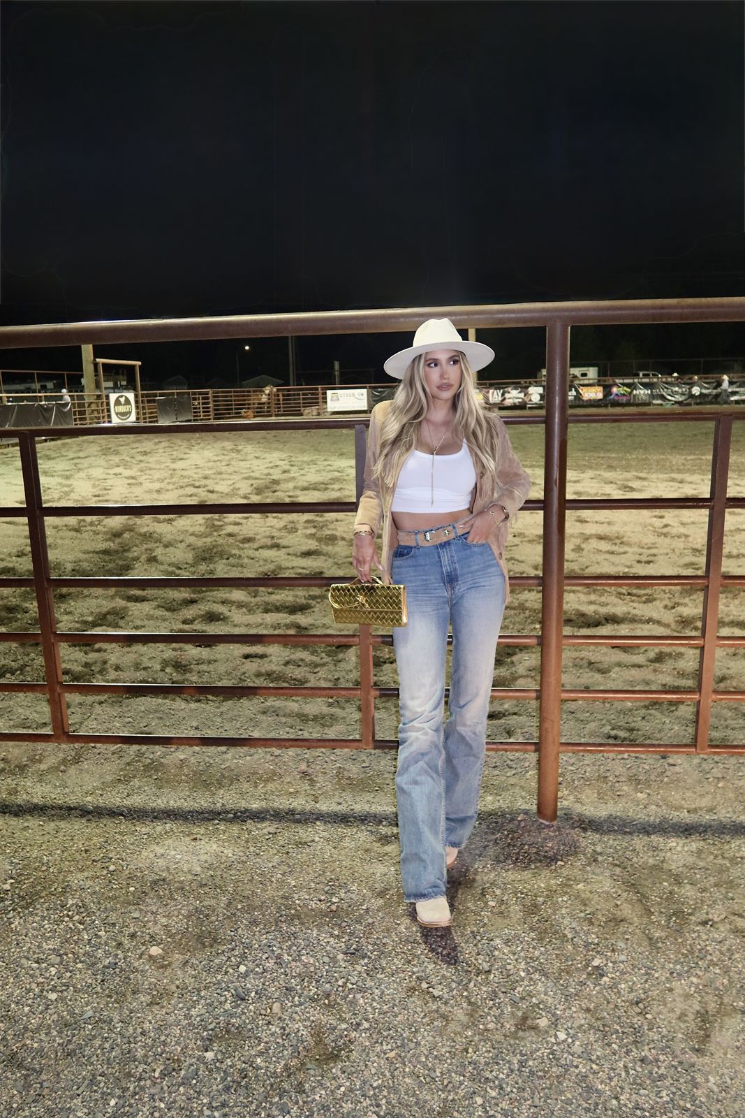 Cream hat, suede fringe jacket, white crop top, vintage denim and a gold clutch at a rodeo arena