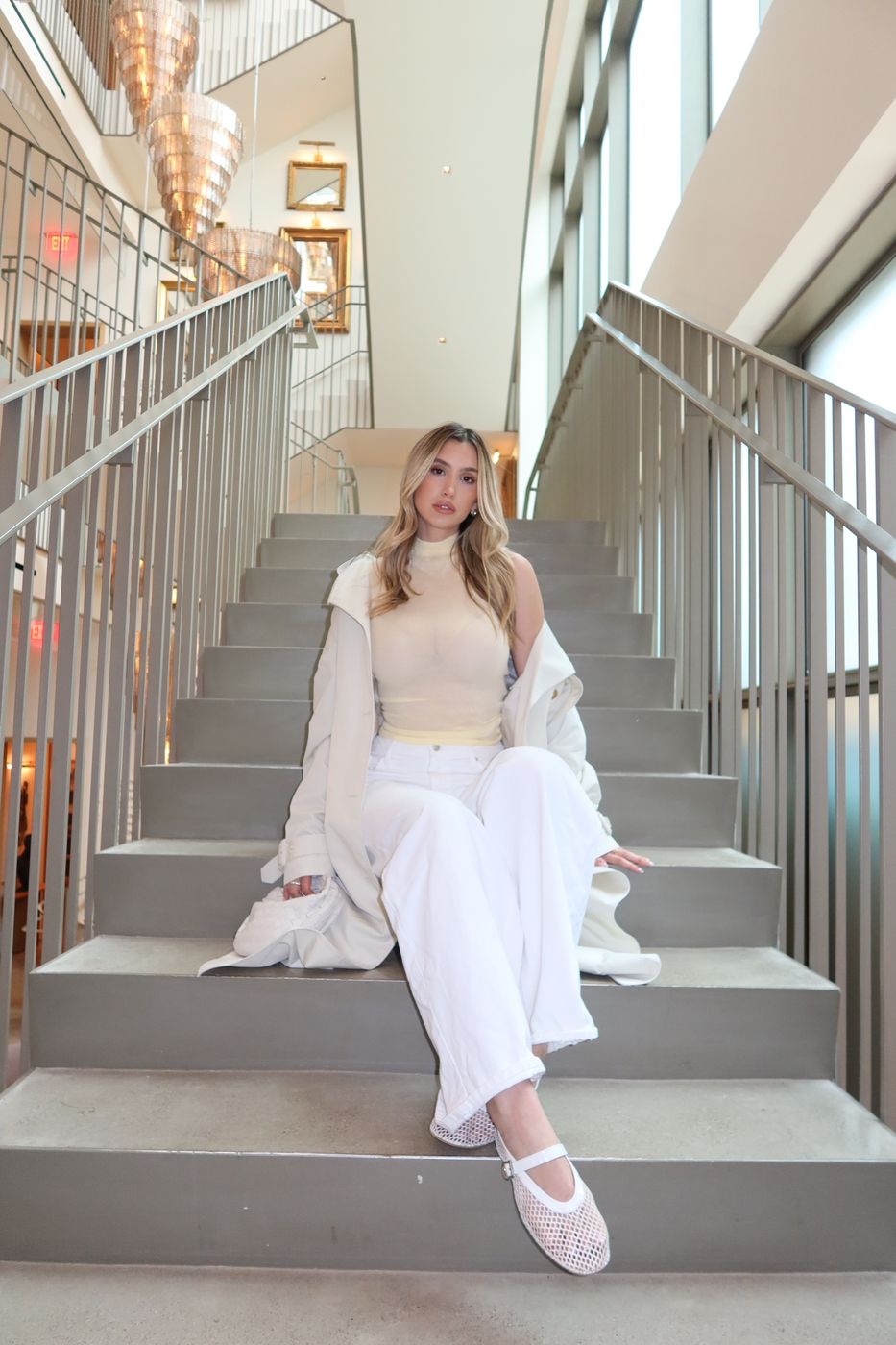 All-ivory look with trench on hotel stairs